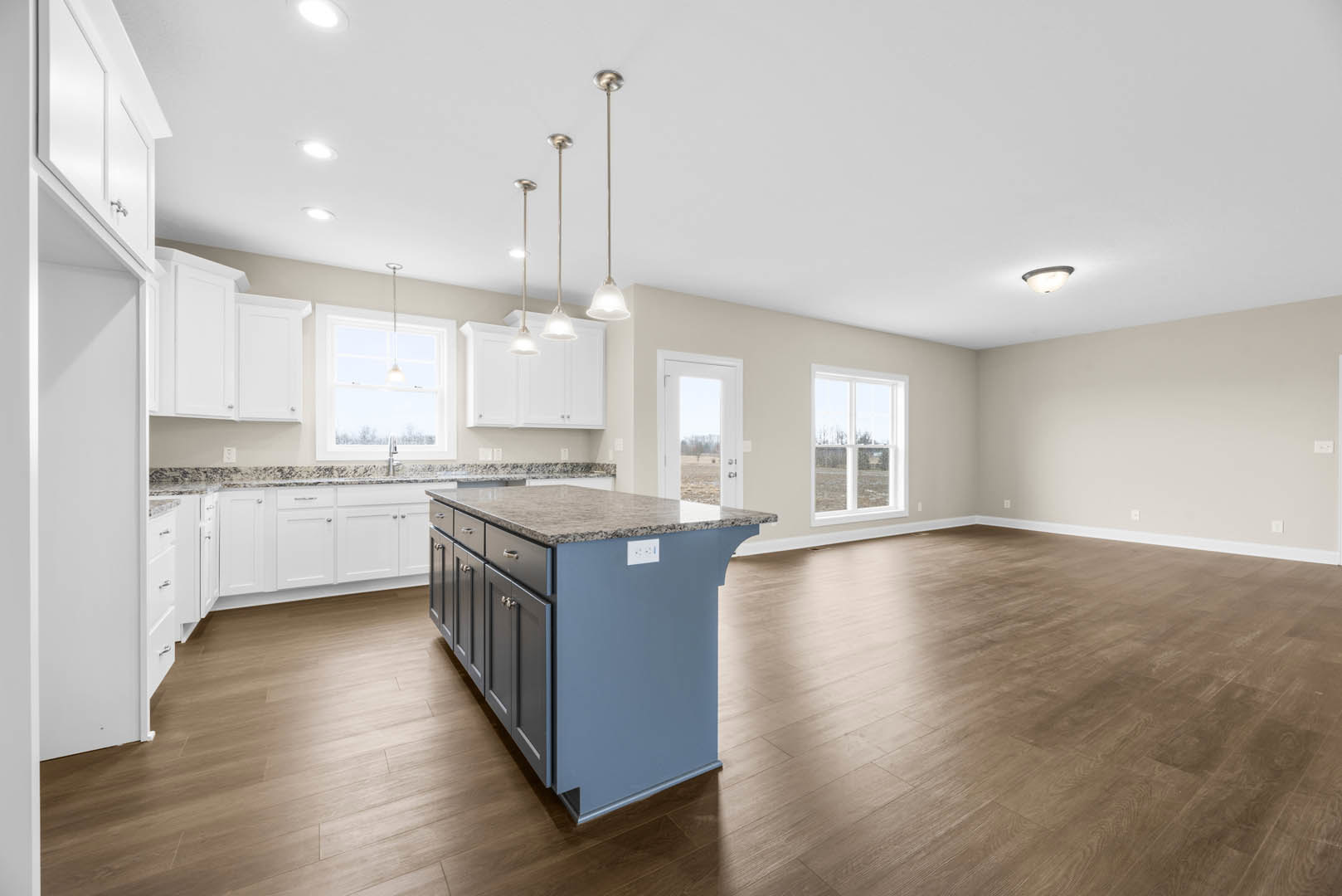 Kitchen with hardwood floors, central island featuring granite countertop, white cabinetry, stainless steel appliances, large window allowing natural light, white door opening to