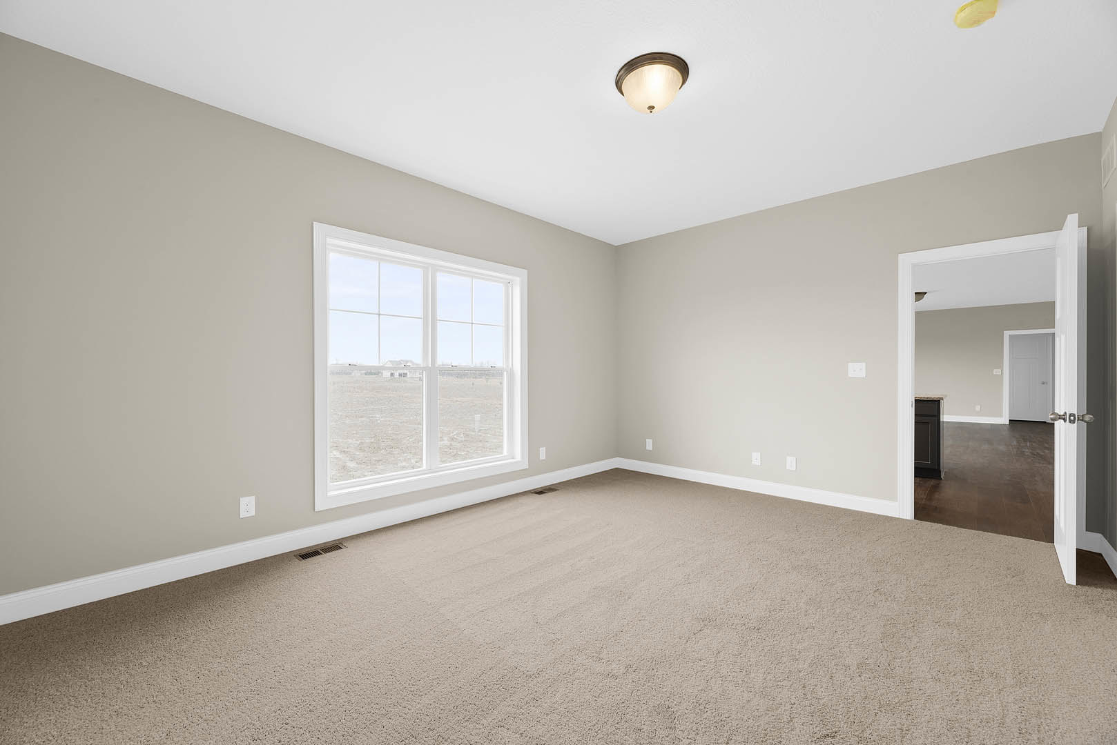 Carpeted room with white walls, open white door with silver handle, large window overlooking grassy field, ceiling light fixture, crown molding along ceiling.