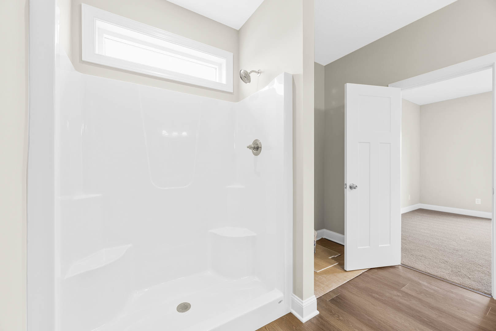 Modern bathroom featuring a white tiled shower with wall-mounted showerhead, light plaster walls, wood door, and neutral flooring