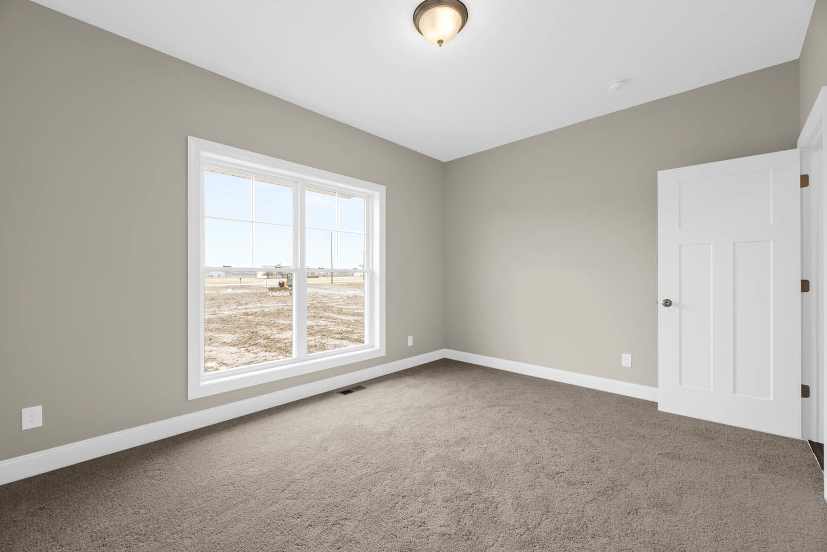 Bedroom with beige carpet, white walls, large window overlooking grassy field, white door with silver handle, modern ceiling light fixture, and white electrical outlet
