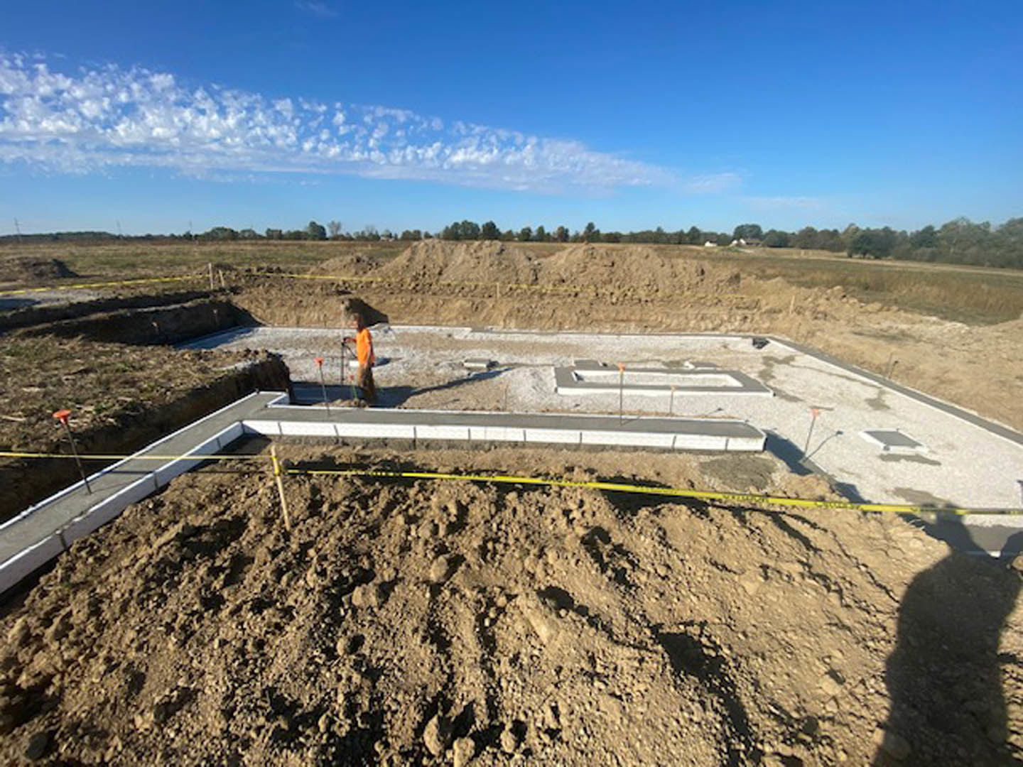 Man holding a shovel in a dirt yard with patches of grass under a partly cloudy sky