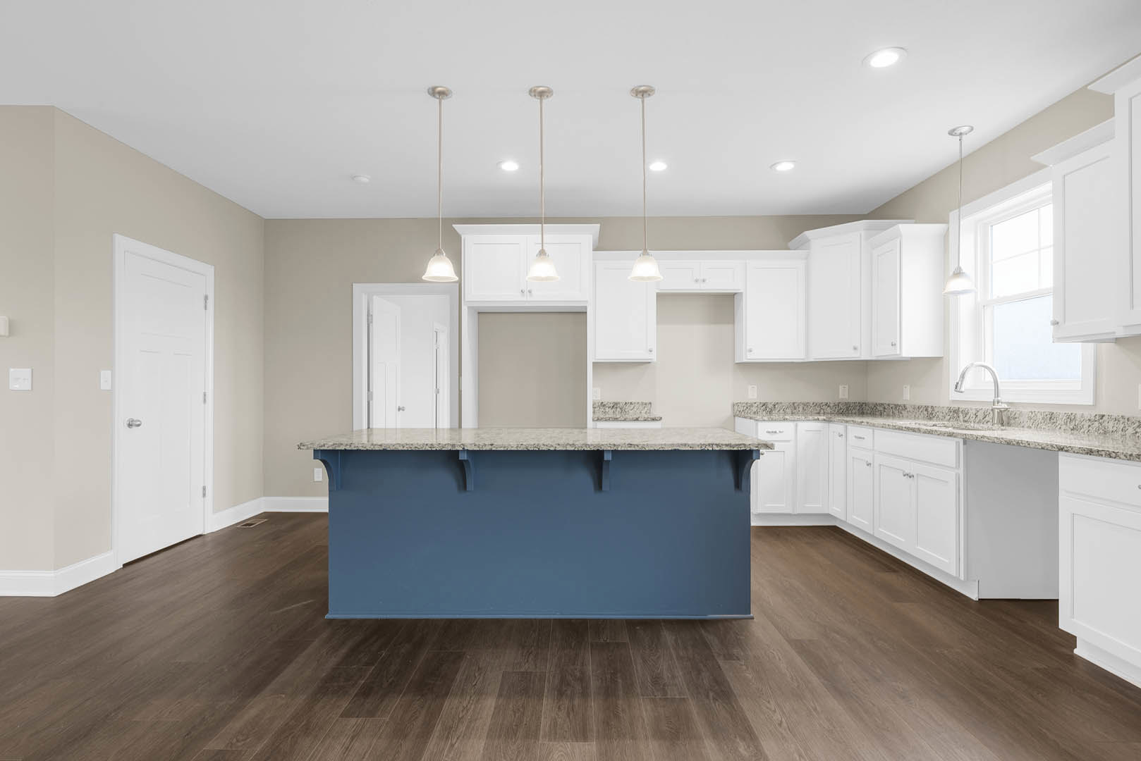 Blue kitchen island with white marble countertop, white cabinetry, wood flooring, blue accent wall, stainless steel sink, silver door handle, white column with black and white