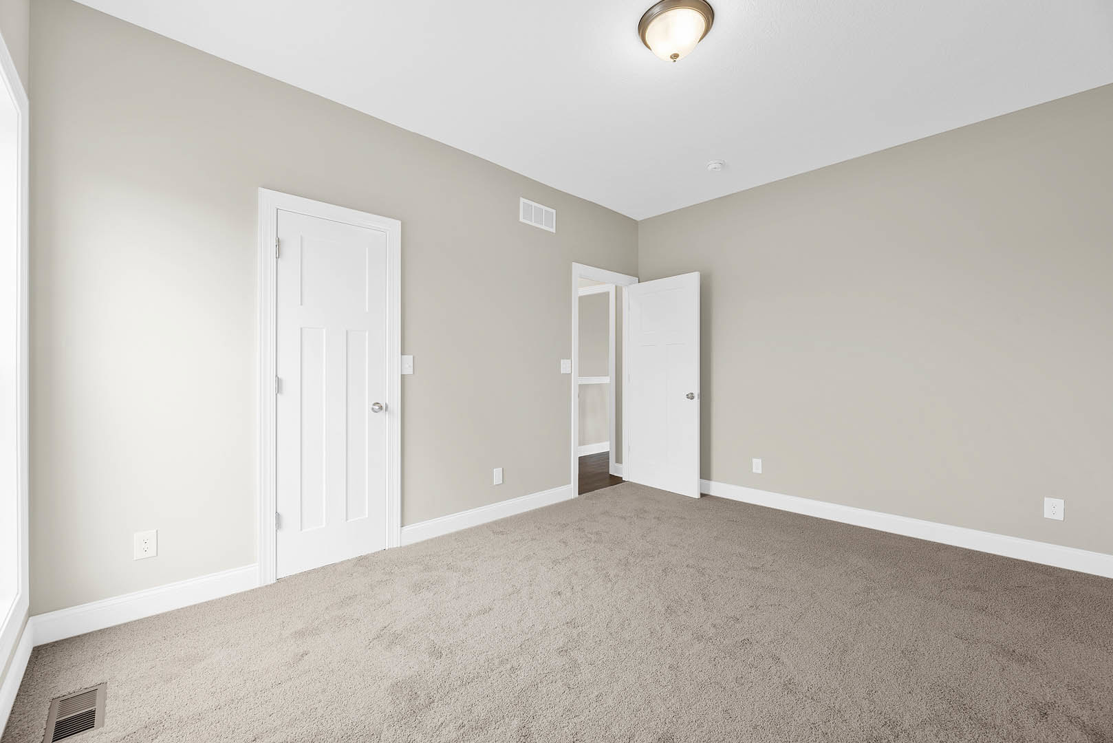 White carpeted room with multiple white paneled doors featuring silver knobs, white walls, ceiling vent, and a modern light fixture.