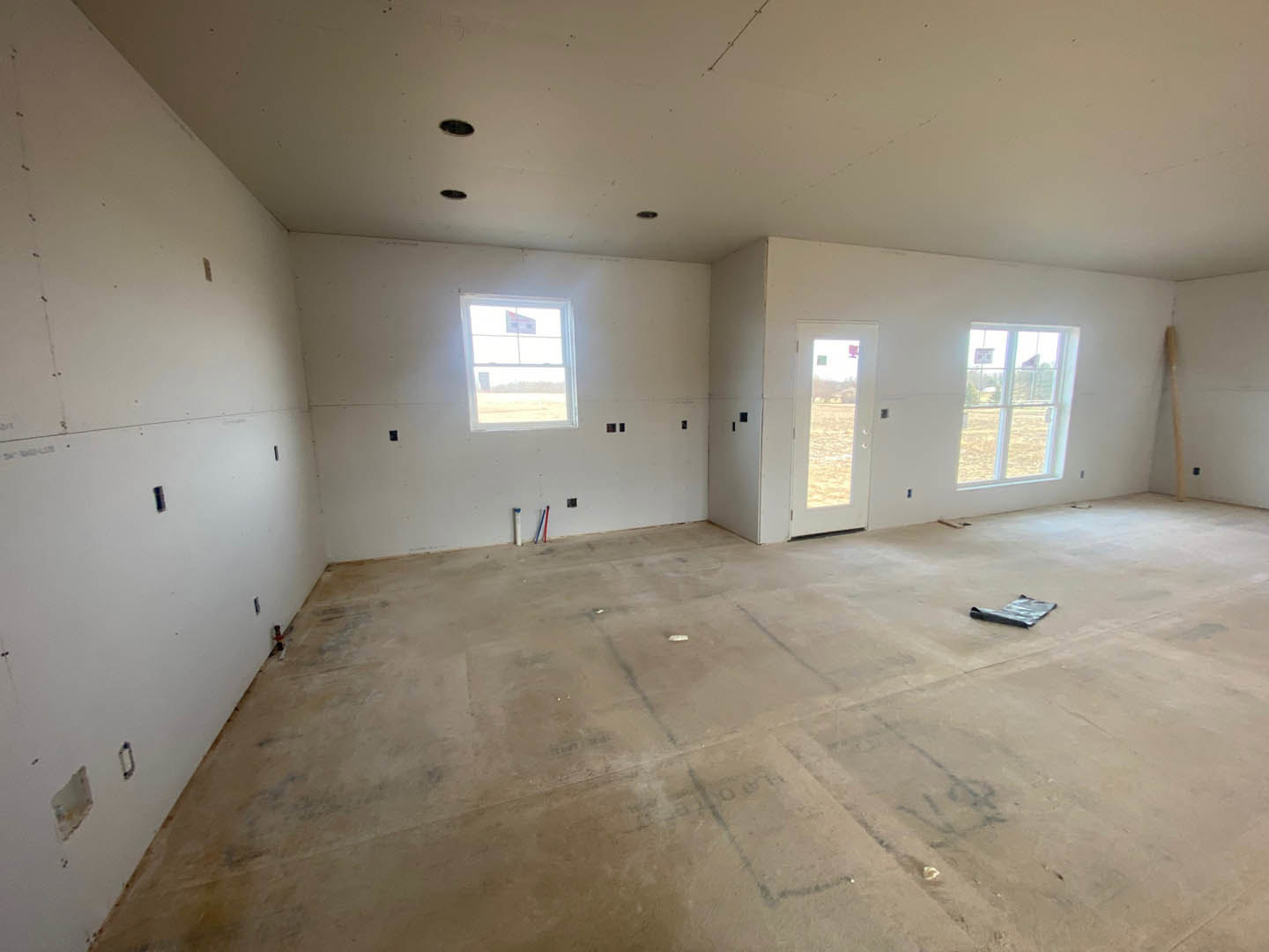 Unfinished room with plaster walls, concrete floor marked with black lines, multiple windows, and a door; ceiling features a visible hole.