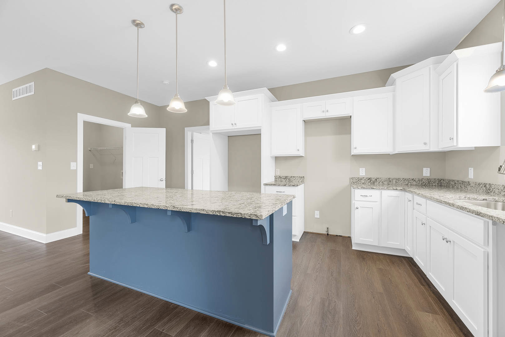 Blue kitchen island with white countertop, white cabinetry, stainless steel appliances, light fixtures mounted on white poles, vent on wall, hardwood flooring, and flag pole with