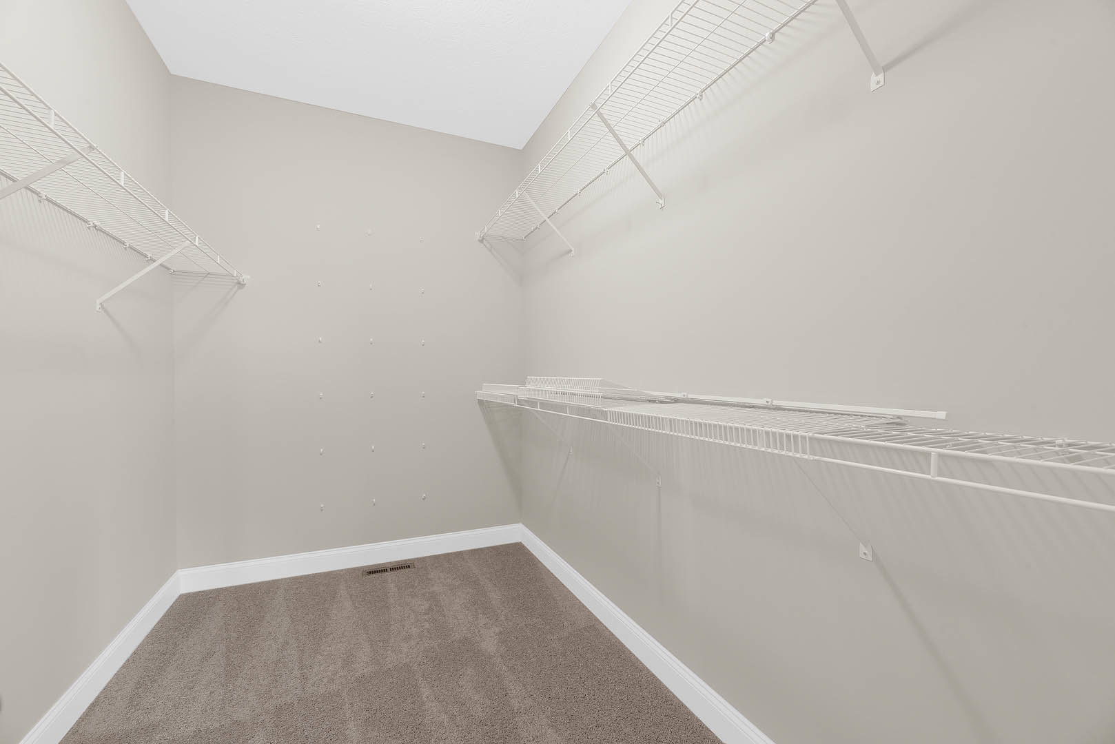 Carpeted room with white wall-mounted shelves and a metal clothes rod, plaster walls, ceiling vent visible
