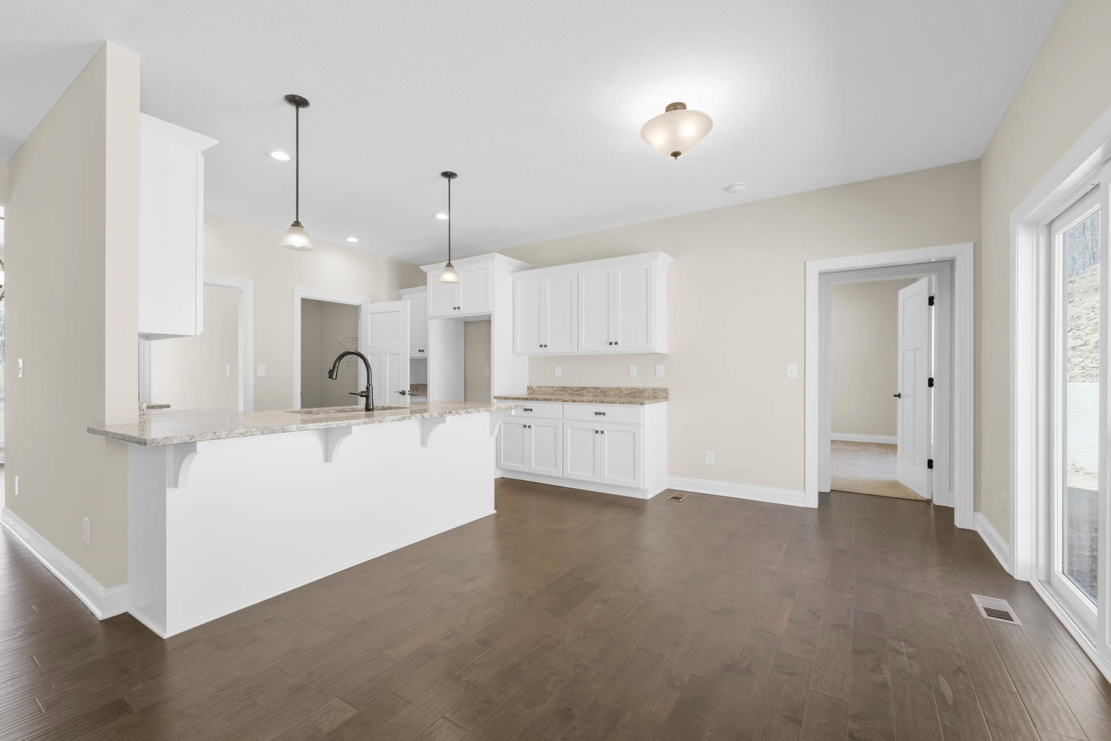 White kitchen cabinets with black handles, marble countertop, hardwood floor, white door, and modern light fixture under plaster ceiling.