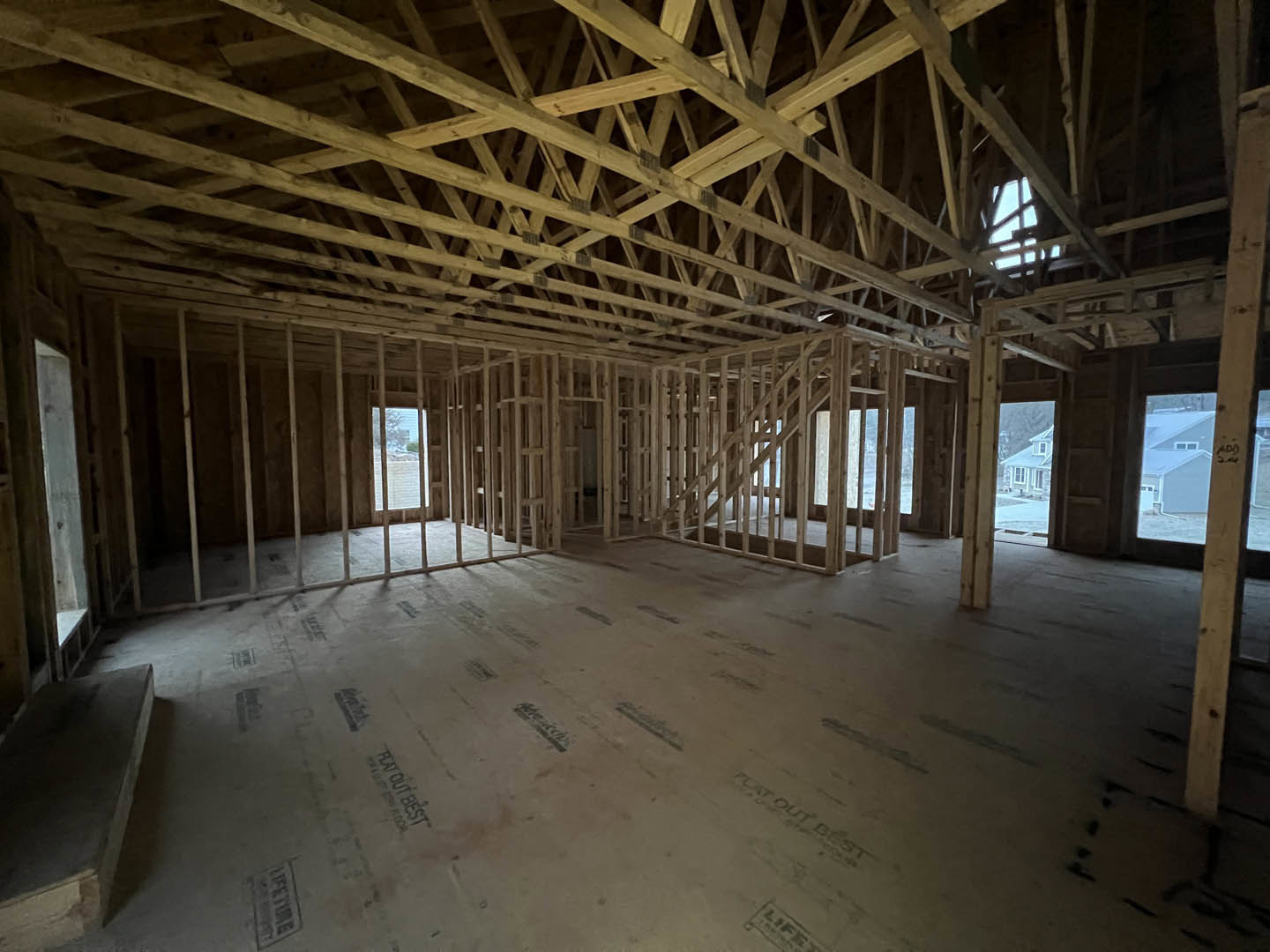 Living room with exposed wood ceiling beams, hardwood floors, large window overlooking a lake, and staircase with wooden railing.