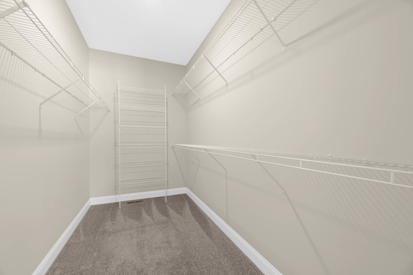 White wire shelving mounted on a plaster wall above beige carpet flooring in a symmetrical indoor room.