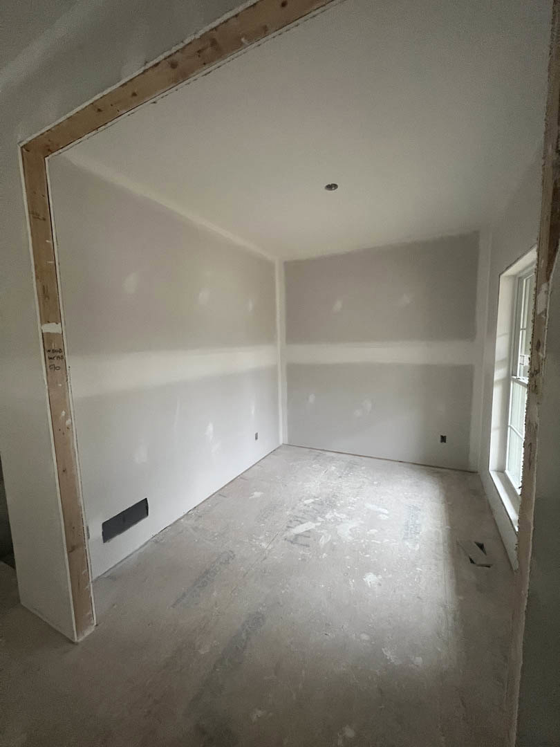 Spacious room with white plaster walls, doorway, large window, light wood flooring, and smooth white ceiling