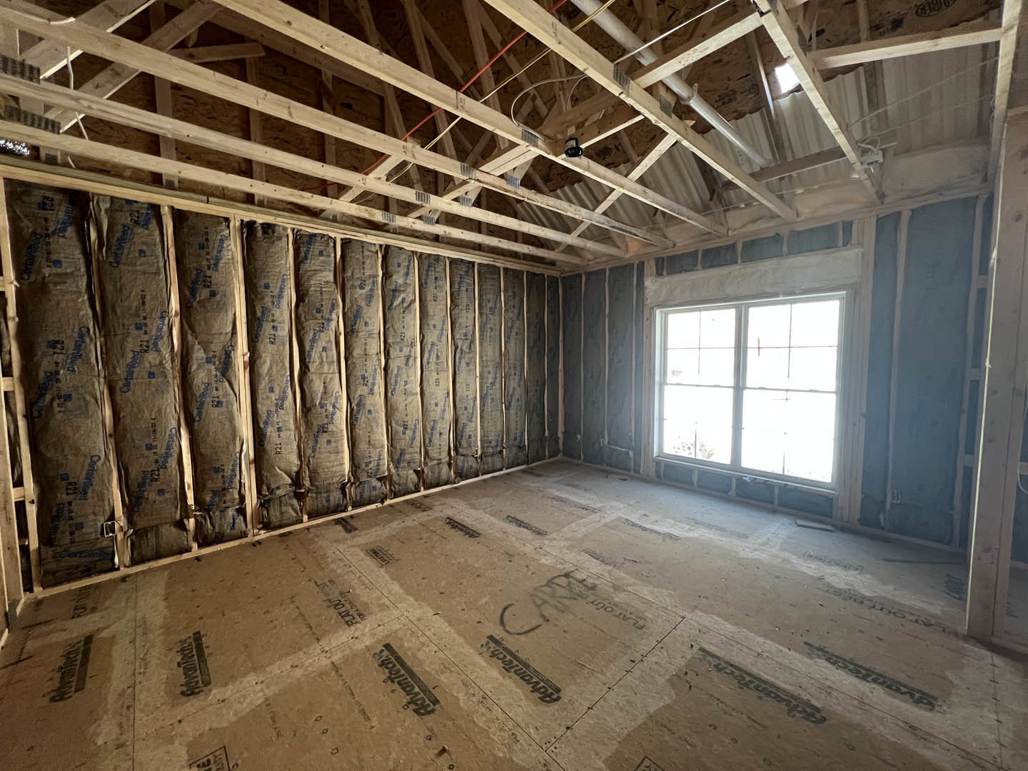 Exposed wood ceiling beams, plaster walls, large window, bags of insulation stacked along one wall
