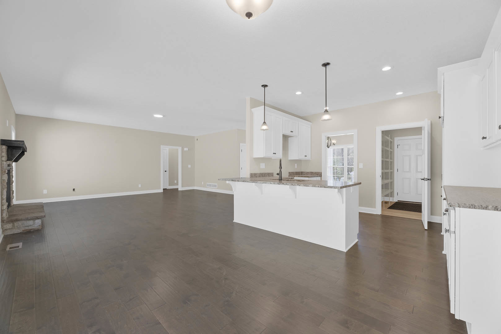 Open-concept kitchen and living room with hardwood floors, white walls, marble countertop, glass shelves, stone-framed accent wall, and white door with black knob