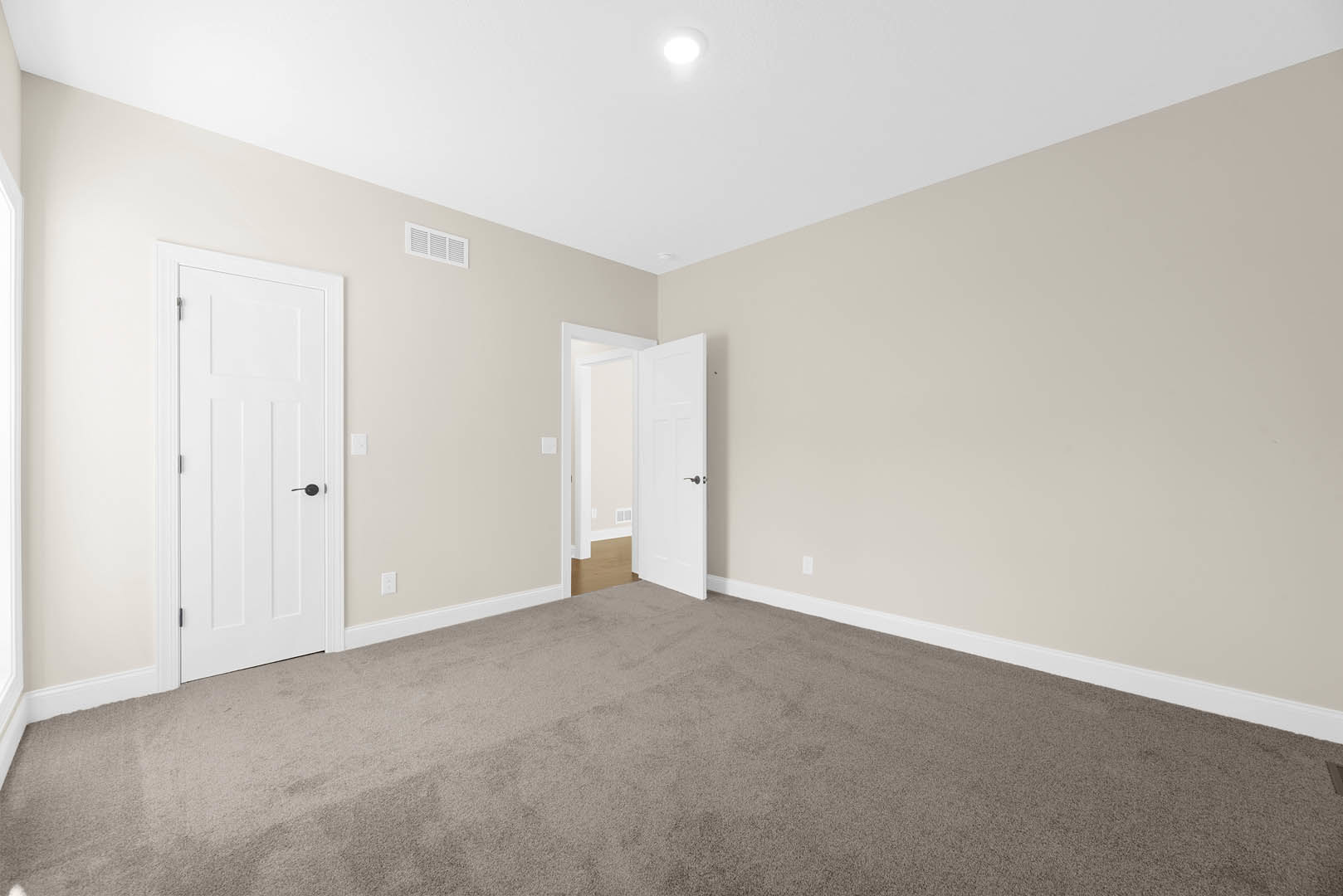 Carpeted room with white paneled doors, black handles, white walls, and crown molding