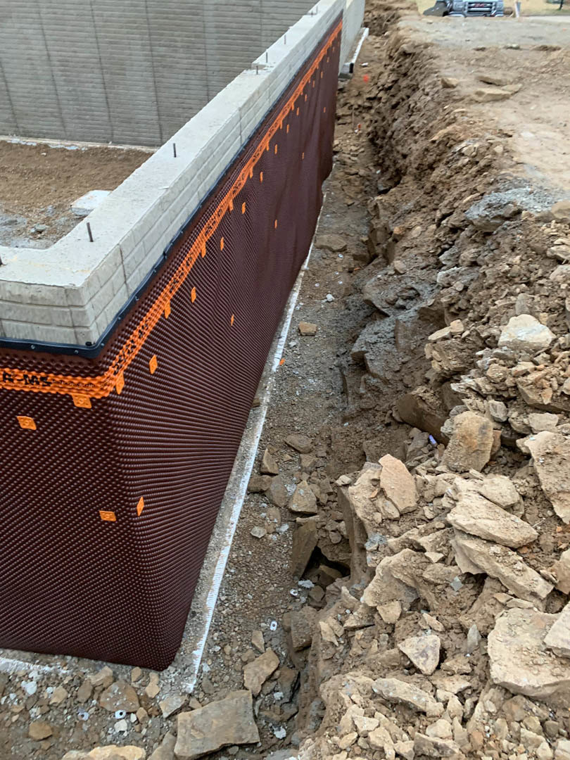 Brick foundation wall with stacked rocks and dirt at the base, outdoor construction site