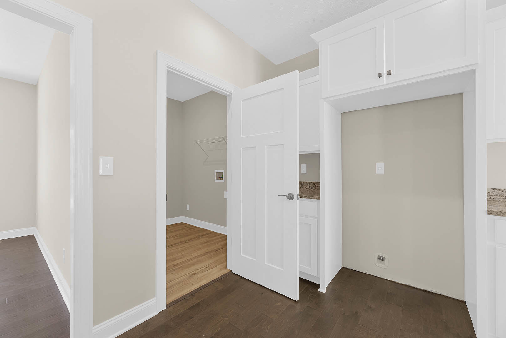 White cabinets along one wall, wood flooring, white walls with matching trim, and a white door with a light switch nearby