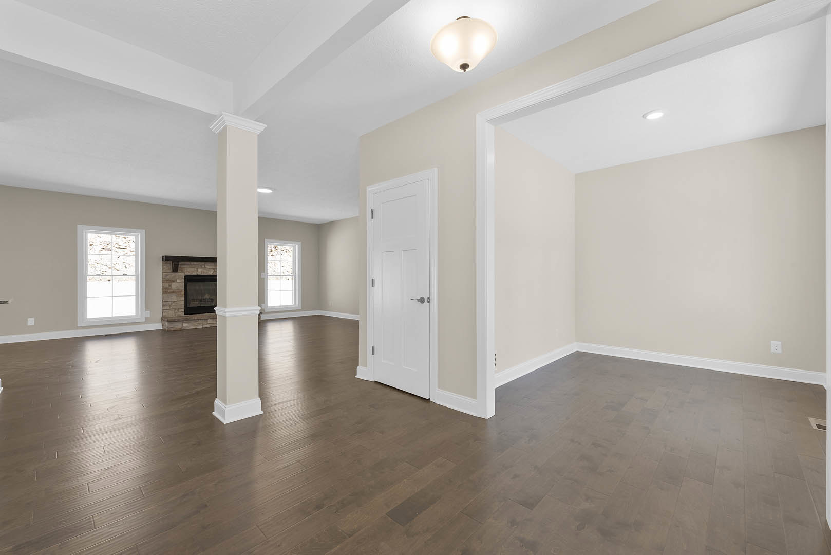 Living room with black-framed fireplace, white door with silver handle, stone accent wall beneath window, wood laminate flooring, and ceiling light fixture