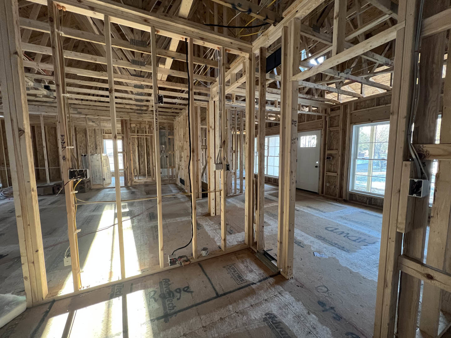 Wood-framed house under construction with exposed beams, unfinished floors, and daylight streaming through a window overlooking a snowy landscape