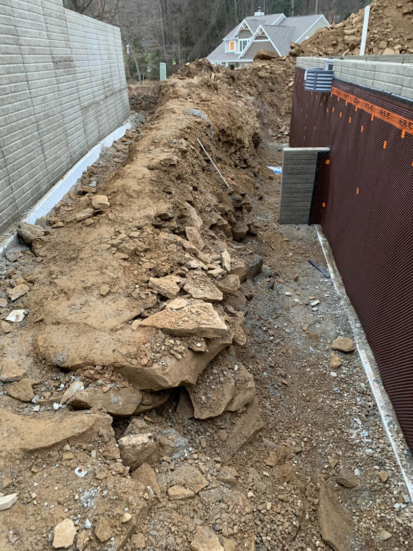 Brown soil and rocks piled near a concrete foundation wall with brick pattern, outdoor residential construction site
