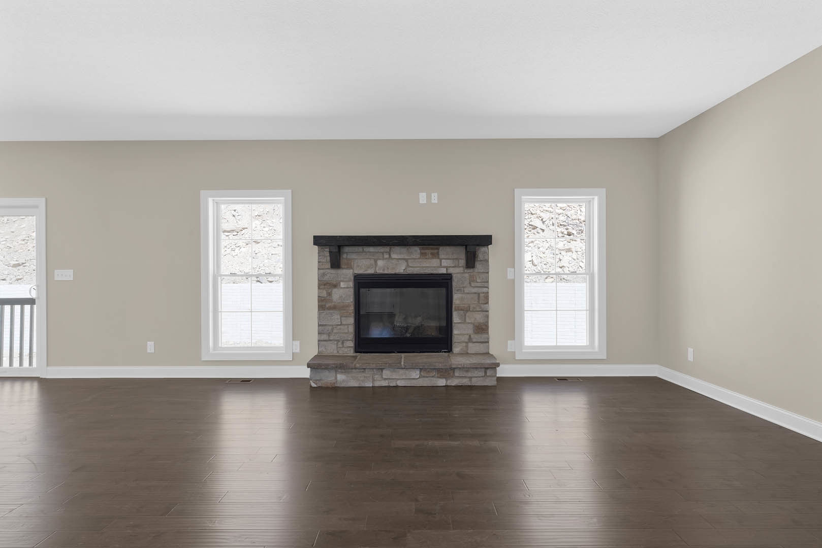 Living room with black-framed fireplace, hardwood flooring, stone accent wall, large glass window and door, white window trim, outdoor view of rocks