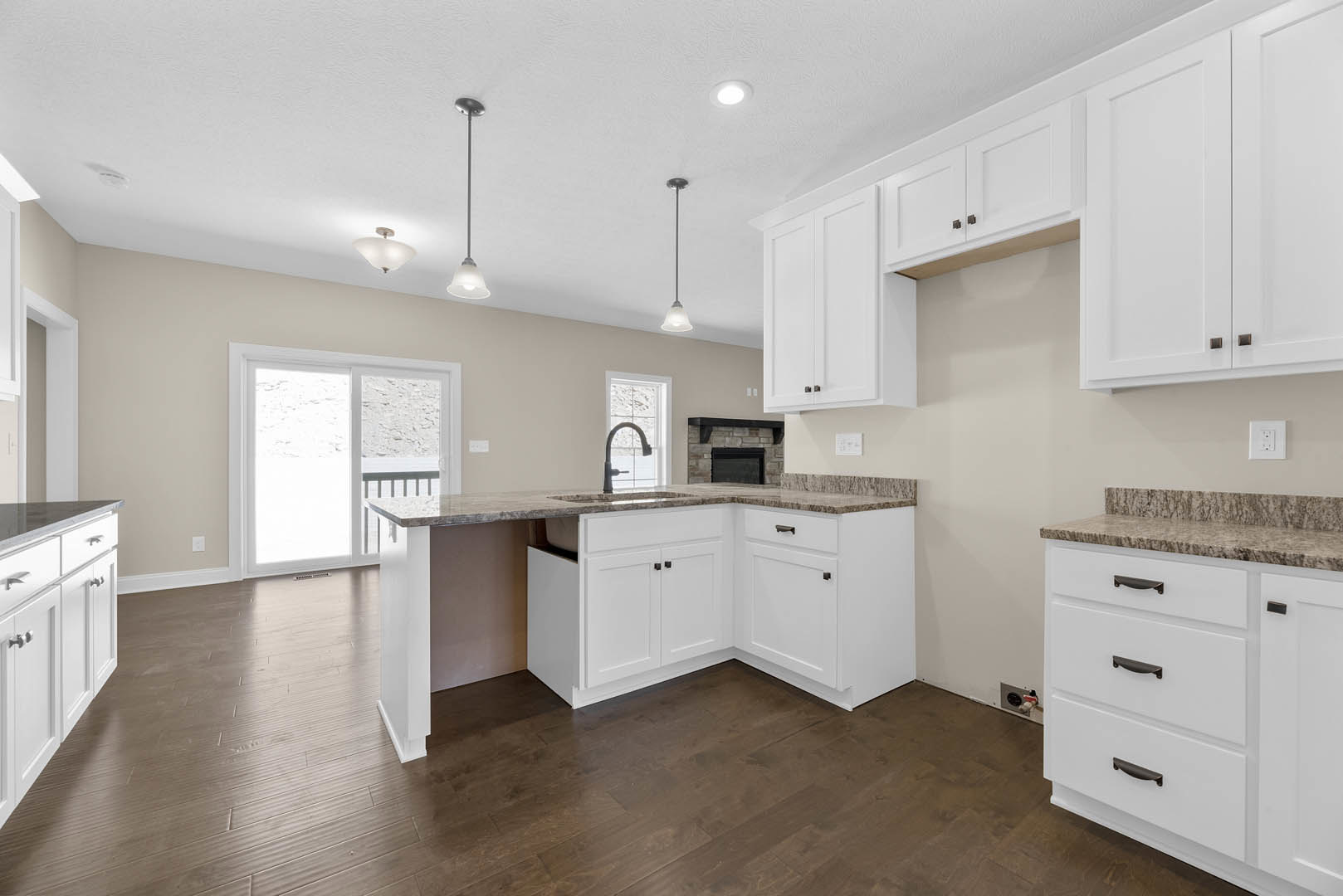 Kitchen with white shaker cabinets, black handles, wood plank flooring, stainless steel faucet, white electrical outlet on wall, sliding glass door, and light-colored countertops