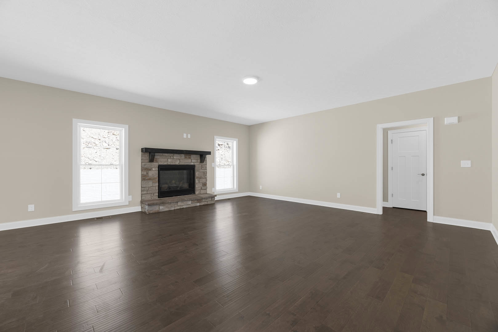 Living room with black-framed glass fireplace, white-framed window, white door with silver handle, and hardwood floors