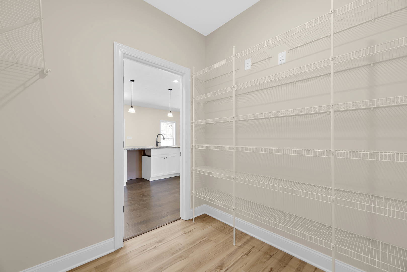 White kitchen cabinet with quartz countertop, white open shelf, wood flooring, and glass door in a bright room with plaster walls and tile accents.
