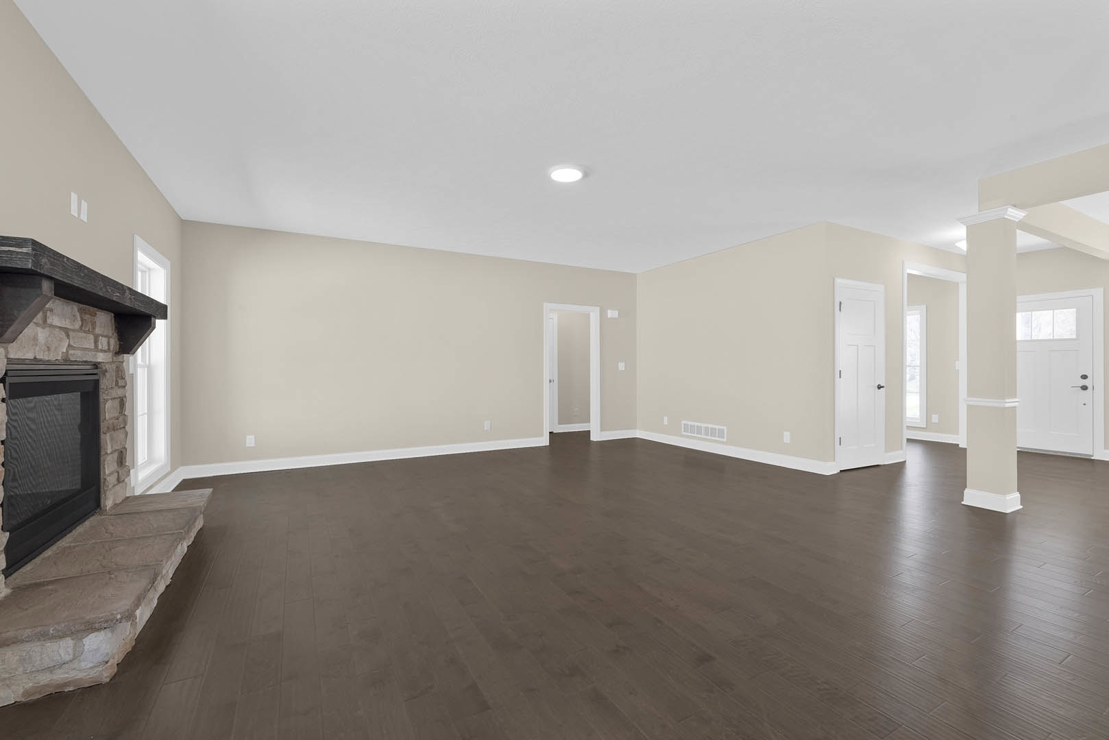 Dark wood flooring in a living room, white door with window and white frame, stone steps beside a fireplace, black screen mounted on wall, plaster walls.