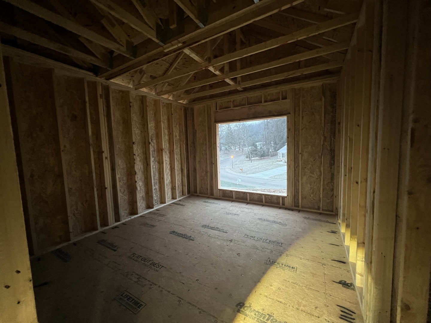 Living room with exposed wood ceiling beams, large window overlooking street, light walls, and hardwood flooring.