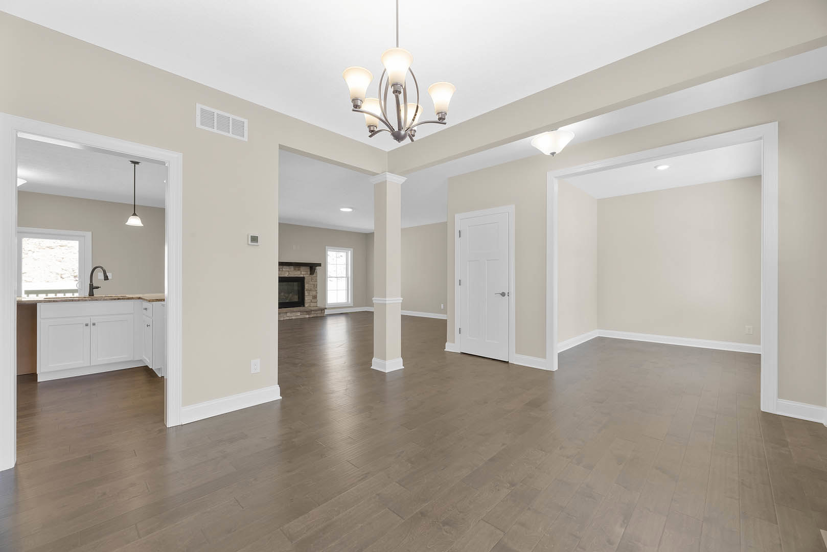 Chandelier hanging from white ceiling, wood flooring, white door with silver handle, white-framed window on brick wall, fireplace with plaster surround, crown molding along walls