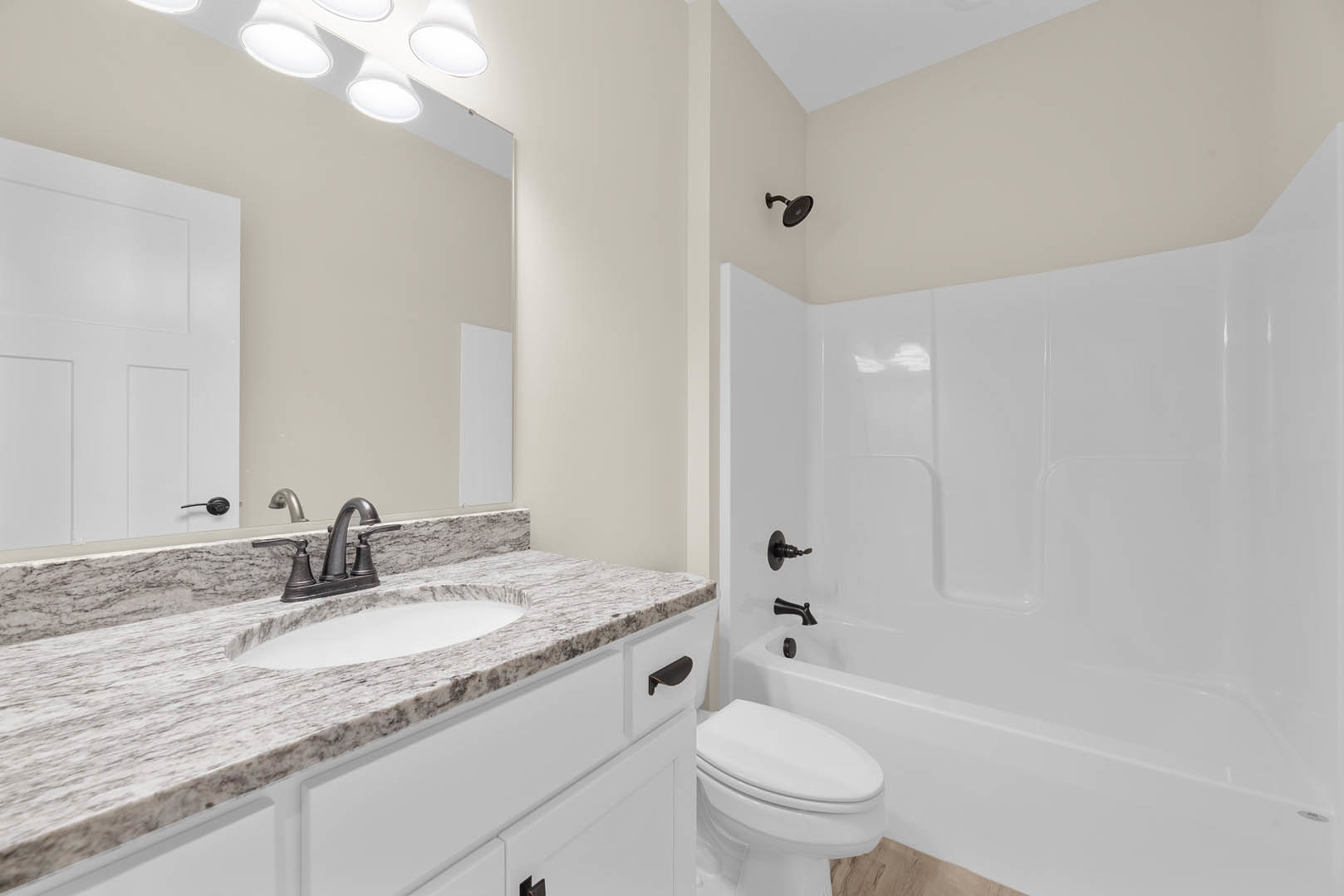 Modern bathroom featuring a white bathtub with black handle, wall-mounted shower head, white sink with chrome faucet, and white toilet; light tile walls and floor, black metal