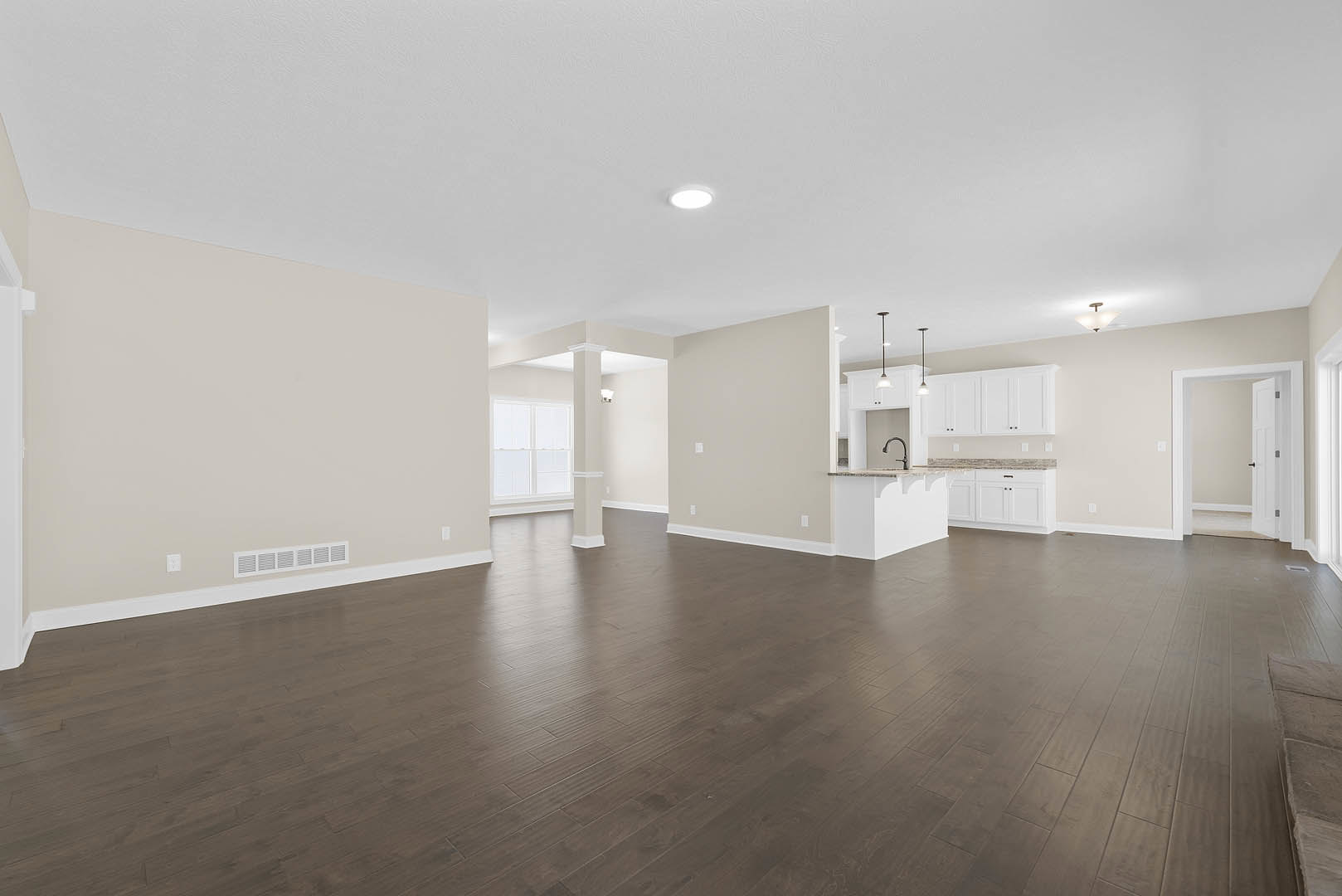 Spacious room with dark wood floors, white walls, white ceiling with recessed light, large window with glass panels, white door with black handle, and marble-topped accent wall