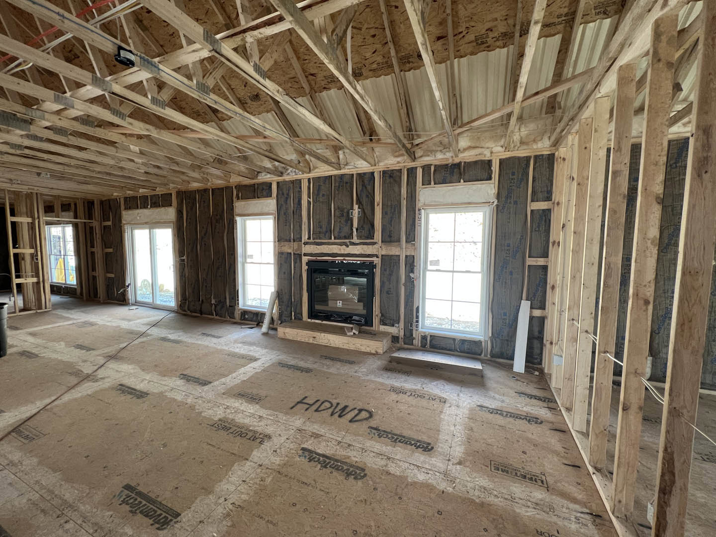Living room with wood beam ceiling, television mounted above stone fireplace, large glass window in wood frame, light-colored floor with black text, modern furnishings.