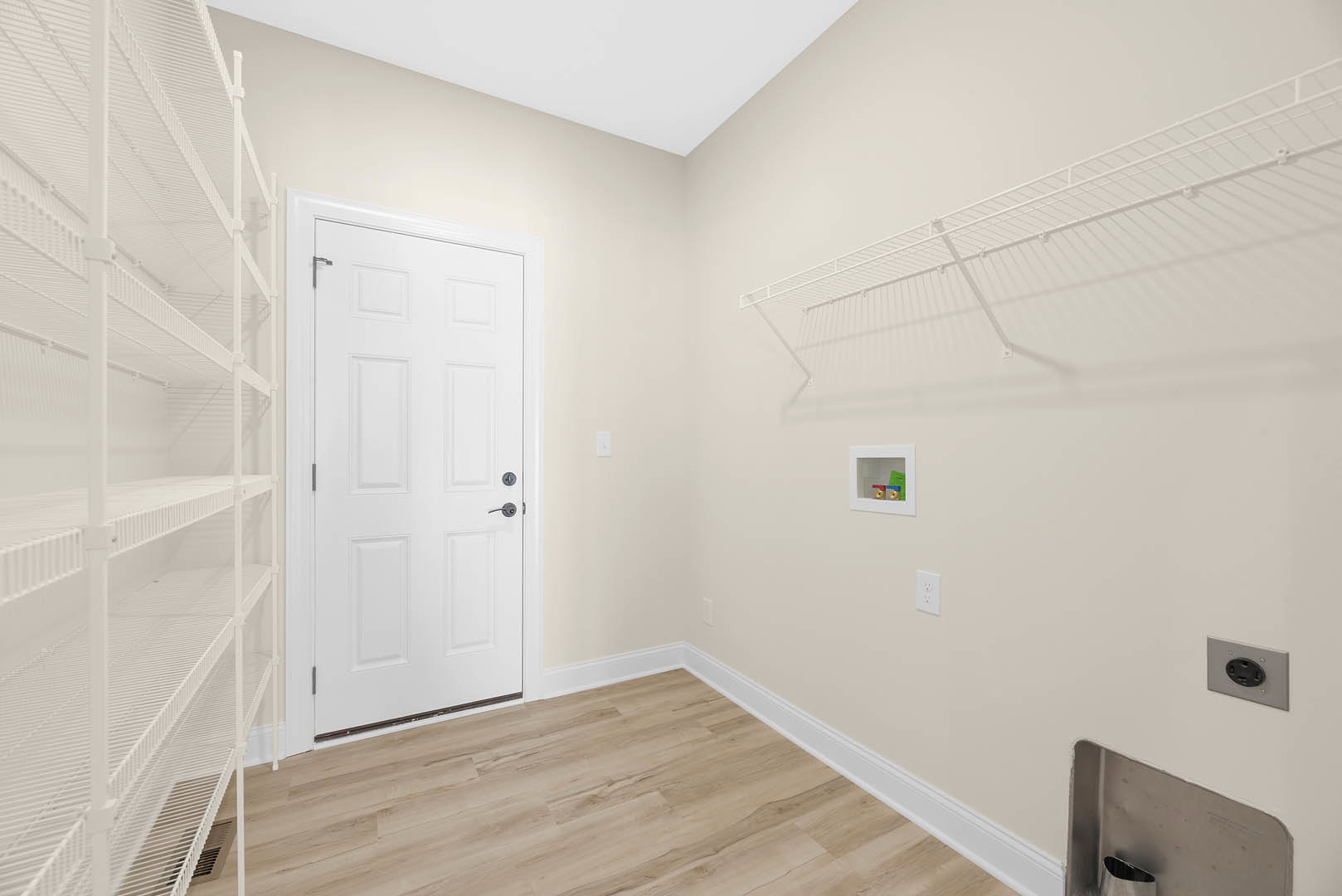 White built-in shelves beside a closed white door with black handle, wood flooring with white baseboard trim, black electrical outlet on white plaster wall, square window letting