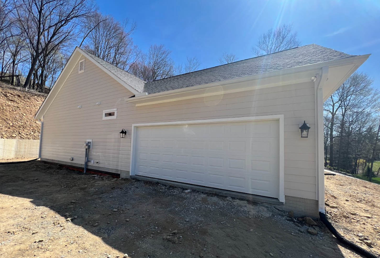 Two-story home with white siding, attached garage featuring a white paneled door, gravel driveway, and a lamp post near the entrance.