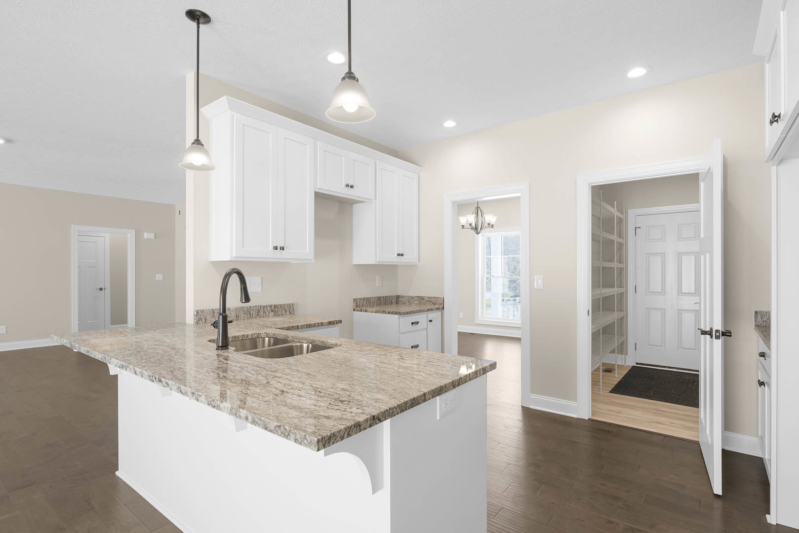Granite kitchen countertop with undermount sink, wood flooring, white paneled door, black metal bar, ceiling light fixture, and tile backsplash