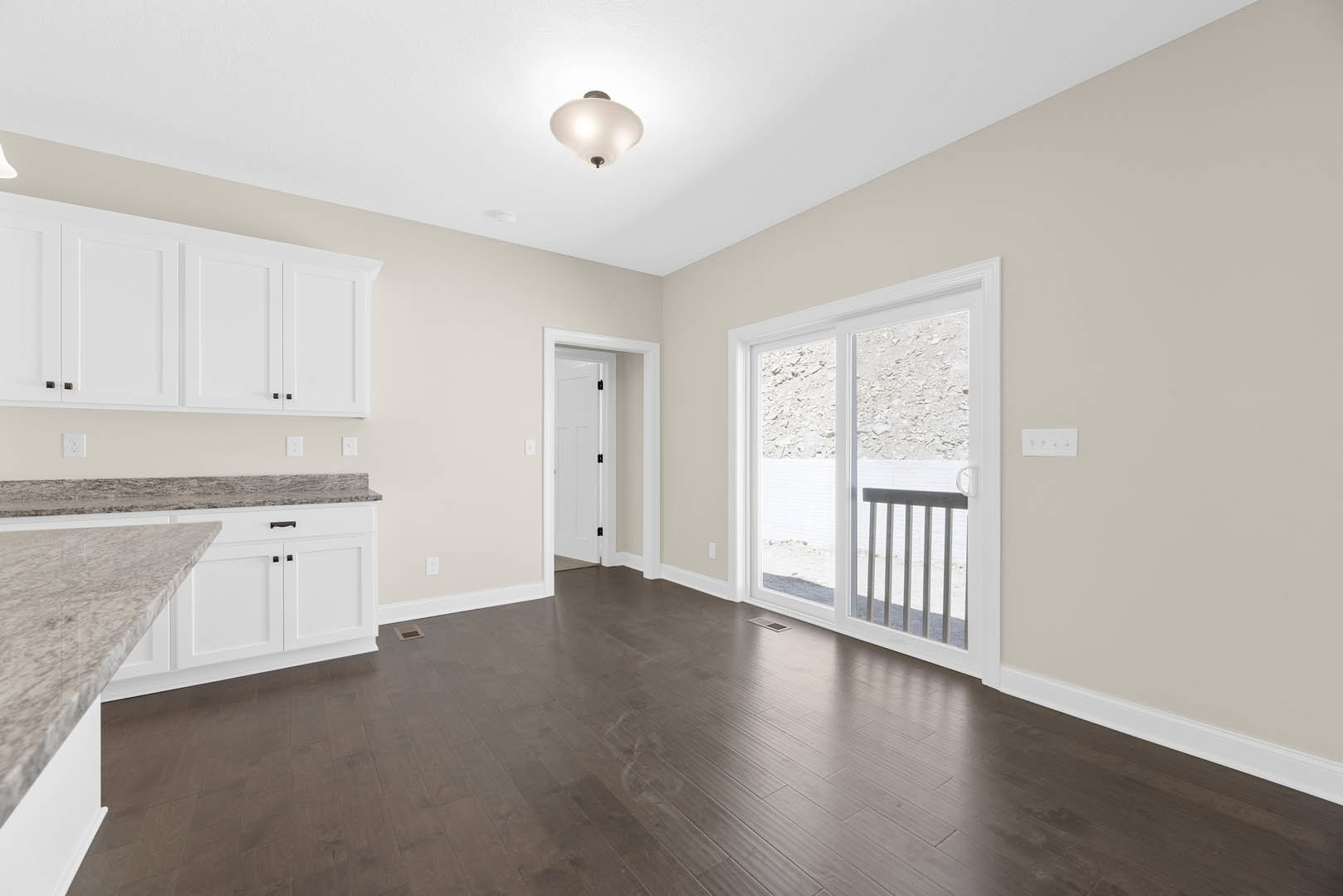 Kitchen with white shaker cabinets, dark wood laminate flooring, quartz countertop, sliding glass door with metal railing, recessed lighting, and plaster walls
