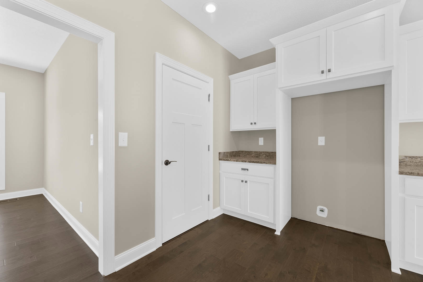 White kitchen cabinets with sleek white countertops, dark wood flooring, white doors, and a wall outlet featuring a green accent.