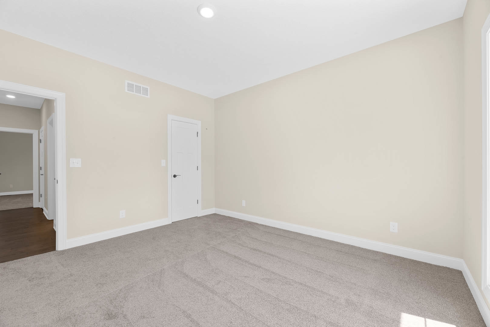 White paneled door with black handle, light gray carpet flooring, white ceiling with recessed light, white walls, dark wood baseboards