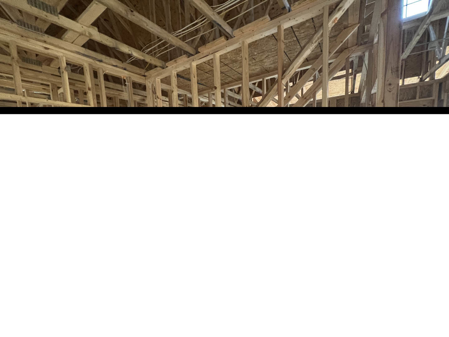 Exposed wooden ceiling beams and rafters with visible wiring, sunlight streaming through a window, white walls in the background