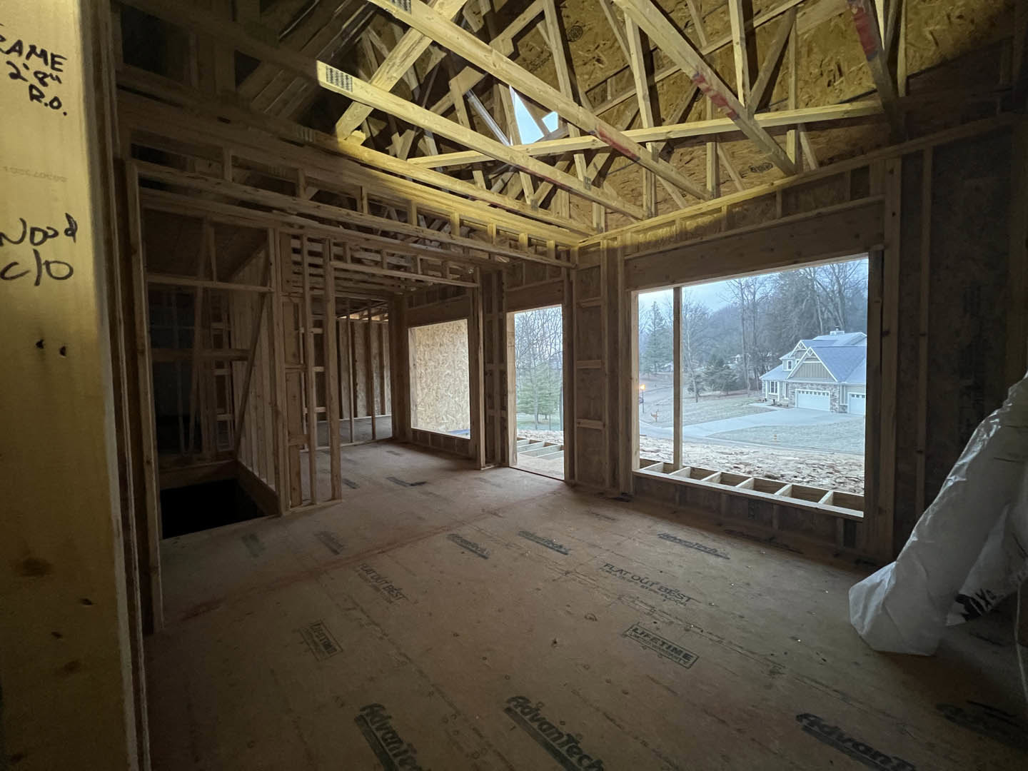 Spacious room featuring exposed wooden ceiling beams, large window with daylight streaming in, unfinished walls, and concrete floor under construction.