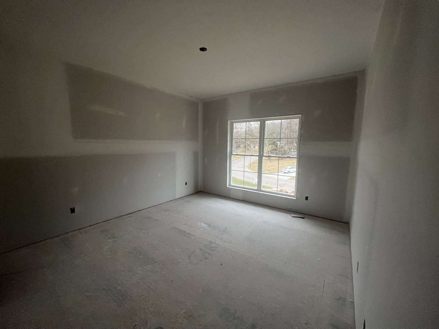 Modern room with two large windows, concrete floor, plaster walls, and views of trees and street outside