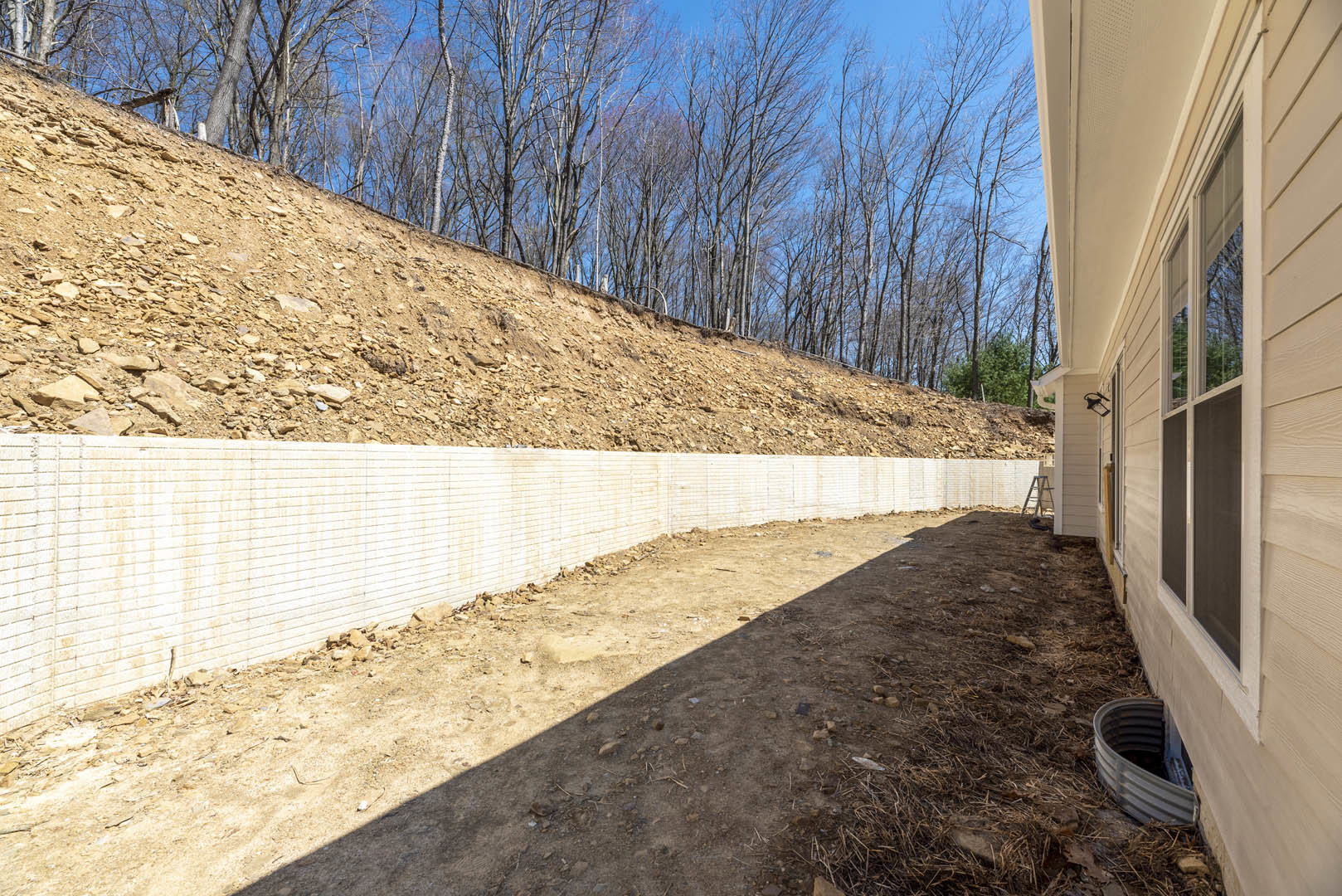Dirt hill with bare trees behind, white and brick retaining walls, metal ground drain, close-up of exterior door