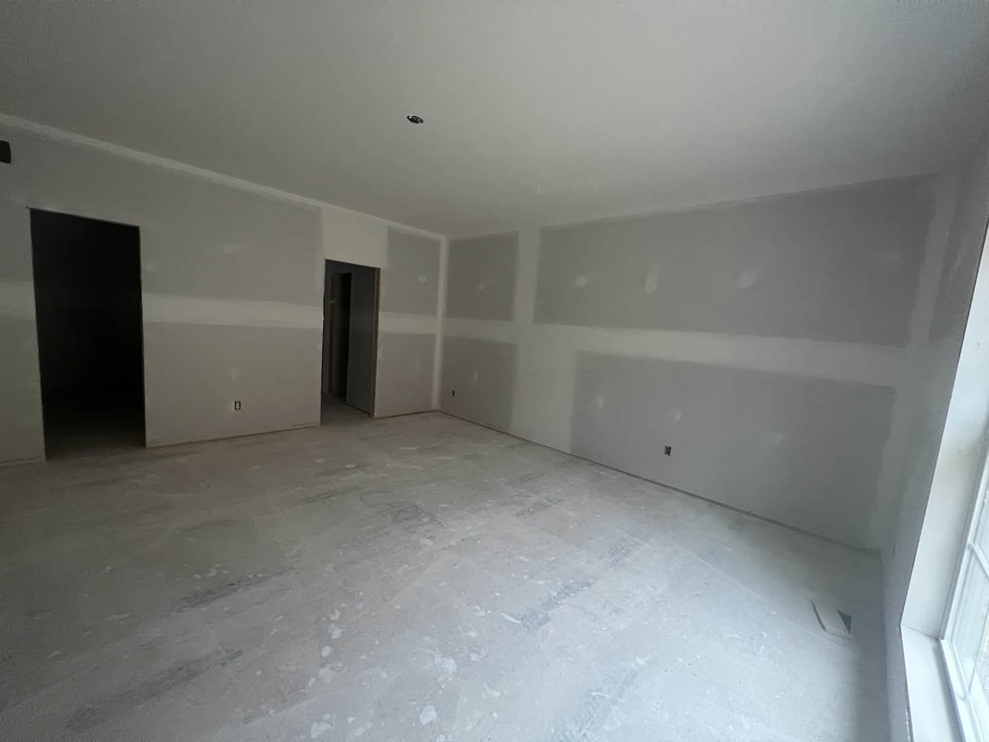 White-walled room with smooth plaster finish, white flooring, and a black-framed door.