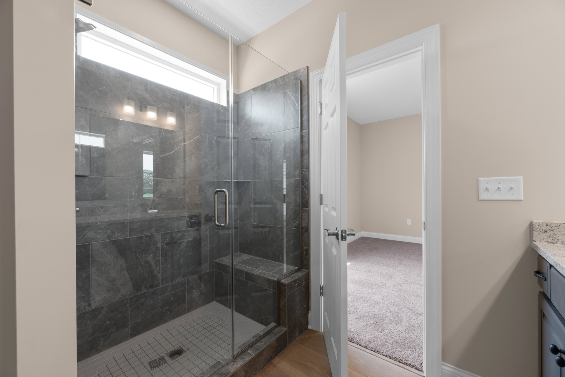 Bathroom with tiled floor, glass shower enclosure, open door leading to adjacent room, wall-mounted light switch, and plaster walls.
