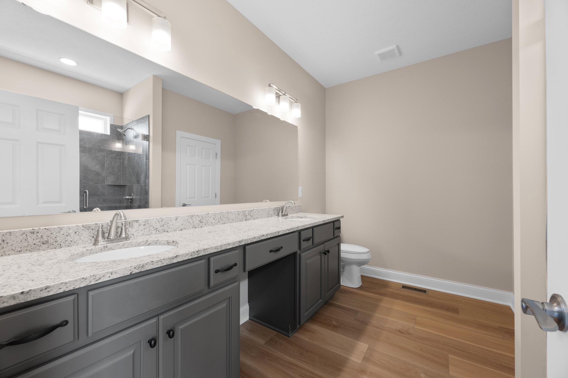 Bathroom featuring marble countertop with undermount sink, white toilet, tiled floor, glass shower enclosure with window, three-light fixture above mirror, white paneled door with