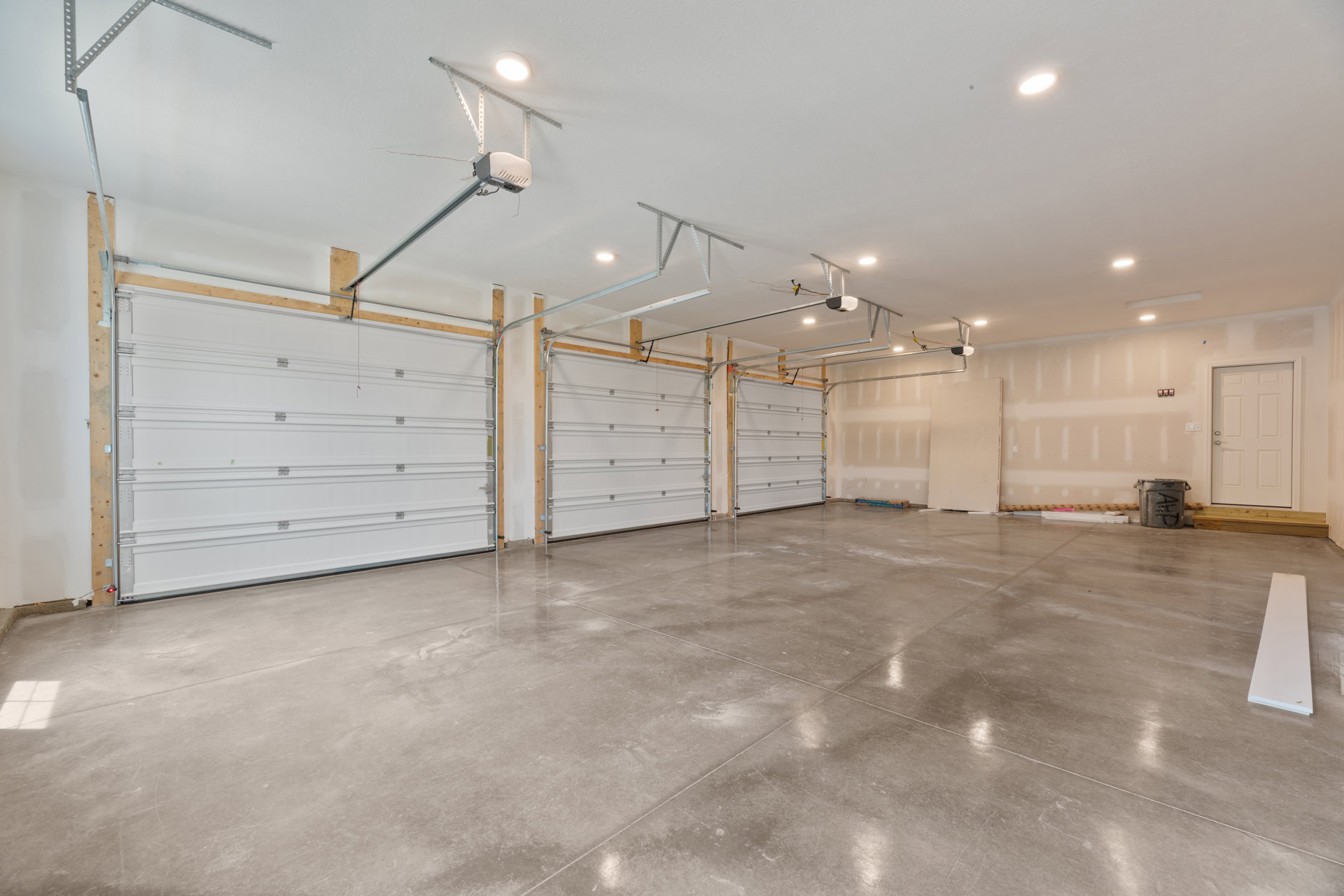 Spacious garage interior with white paneled doors, concrete floor, plaster walls, ceiling light fixture, and wood trim around the main garage door