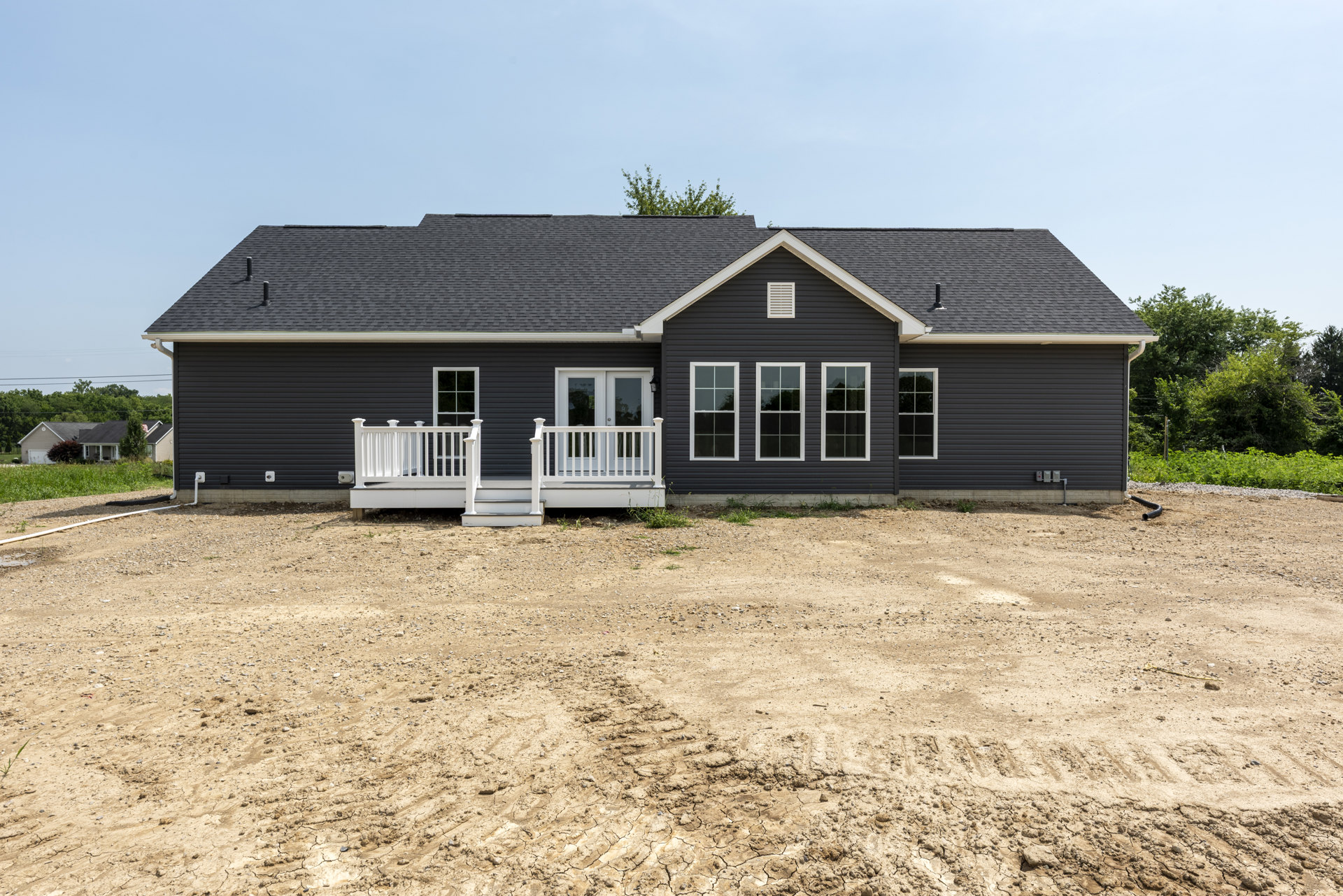Two-story house with white porch railing, white-framed windows, dirt yard with visible tire tracks, and surrounding trees.