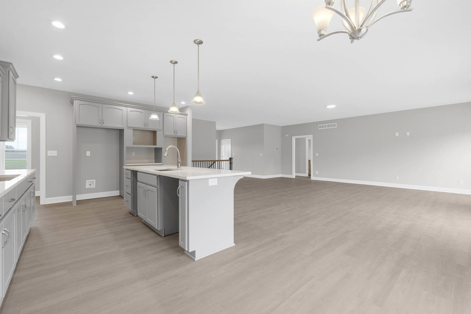 Open-concept kitchen and living room featuring wood laminate flooring, white cabinetry, a kitchen island with sink, white countertops, and modern light fixtures.