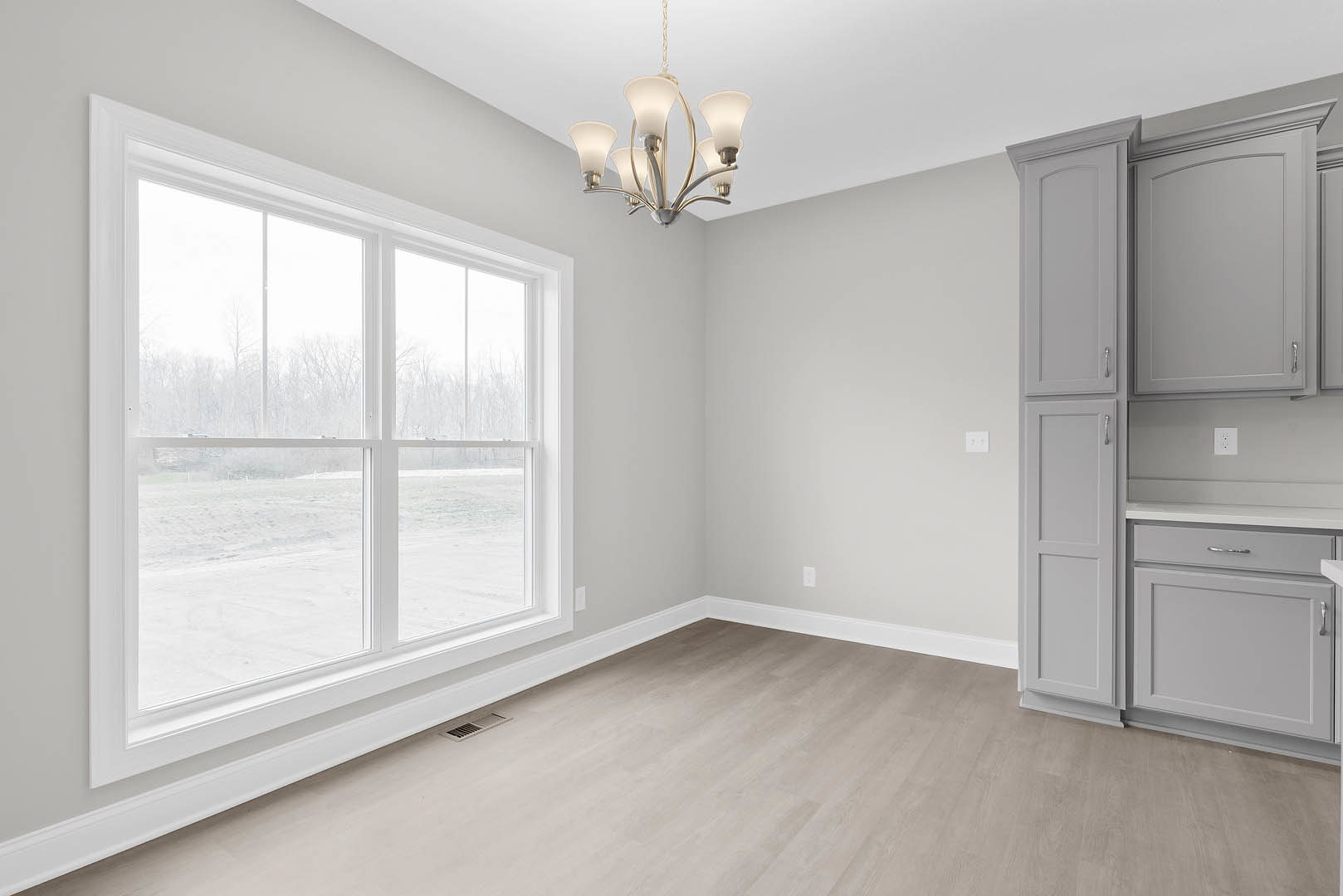 Chandelier hanging above wood flooring, window with white trim, built-in cabinetry, and paneled door in a residential interior.