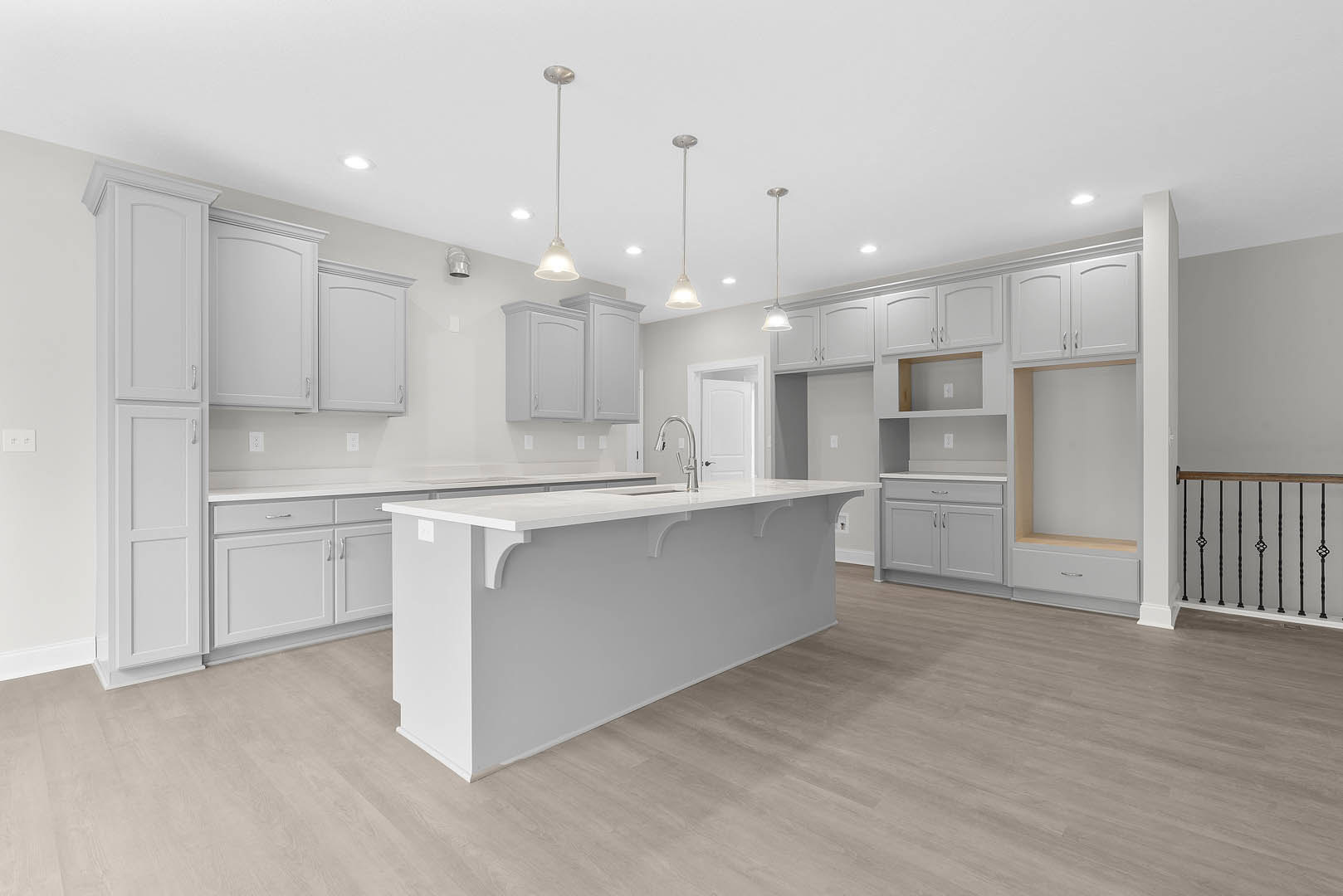 White kitchen with shaker cabinets, silver handles, white quartz island, wood flooring, stainless steel faucet, and white walls